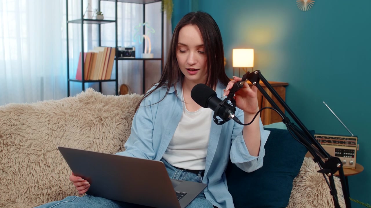 Blogger wanita dengan gembira merekam vlog podcast di sofa sambil dengan aktif memberi isyarat menceritakan kisah yang menarik