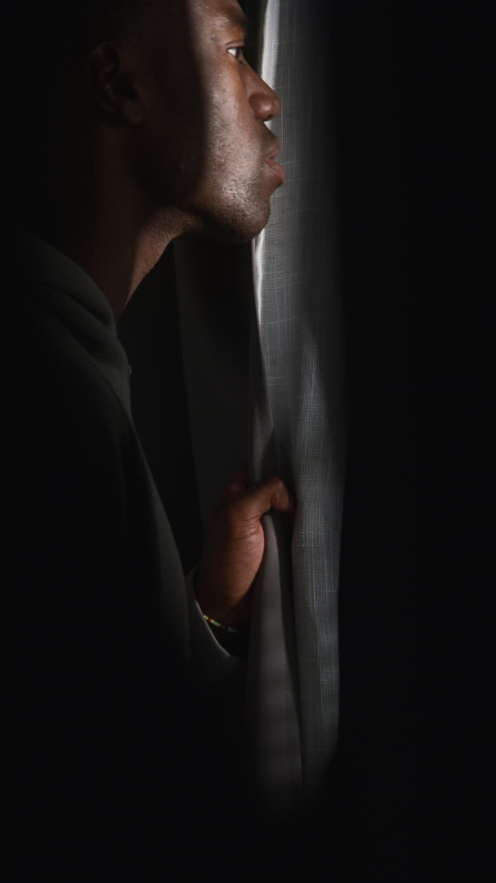 video vertical de un joven infeliz y deprimido en casa mirando por la ventana sufriendo de agorafobia o paranoia 3