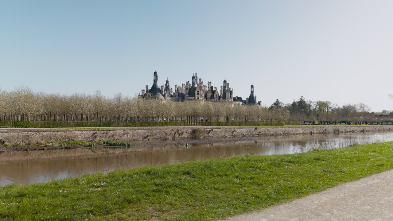 Majestic view of Chambord Castle with canal and trees under clear blue sky