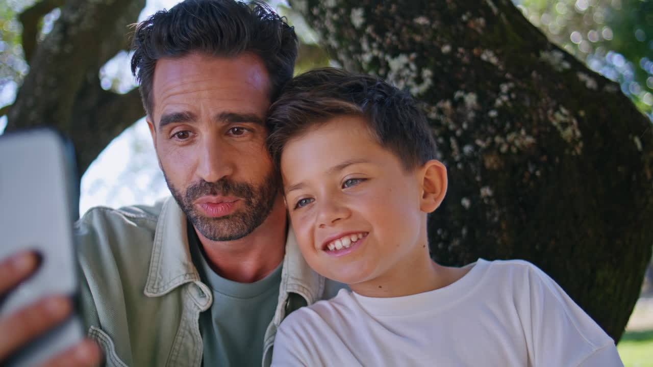 Talking dad boy videocalling on nature using modern smartphone closeup