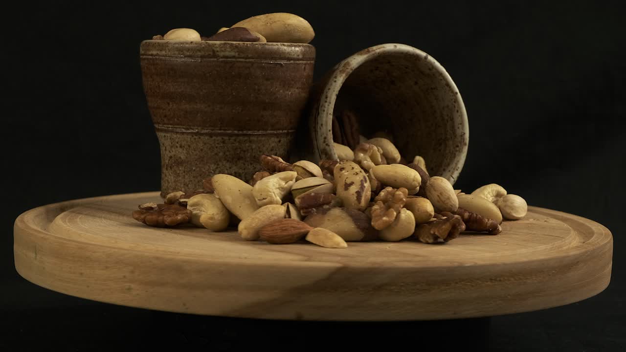 Assorted shelled nuts rotate on board against black background
