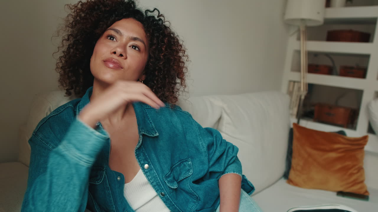 Jovem relaxando no sofá de casa com cabelo cacheado