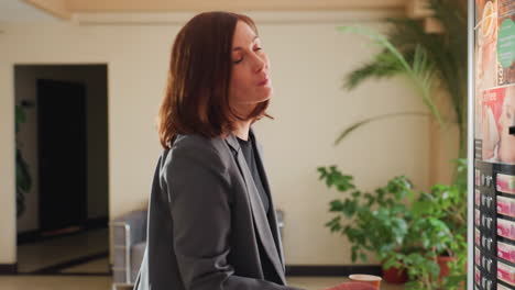 businesswoman standing near vending machine in office, selecting beverage, casual office break, suit attire, choosing drink, modern office, workplace environment, break time refreshment