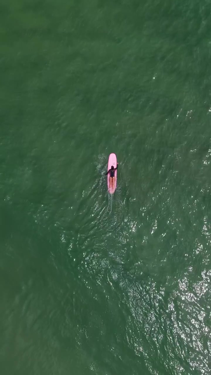 Above View Of A Woman Lying On A Surfboard And Swimming In The Water At My Khe Beach in Da Nang, Vietnam. Vertical, Aerial Shot