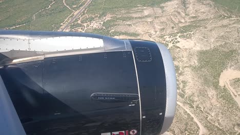 Hand-held-shot-looking-out-of-an-aeroplane-window-looking-to-the-engine-and-barren-landscape