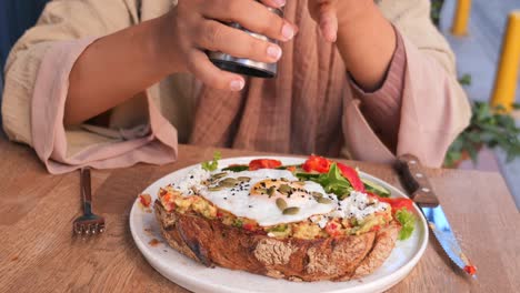 woman eating avocado toast with egg at a cafe