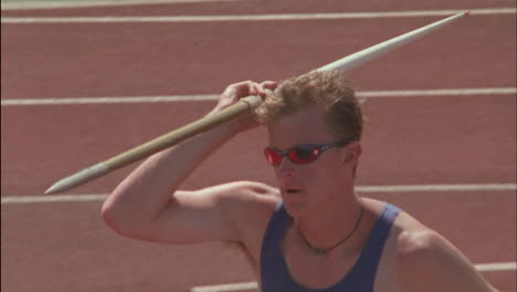 a man runs throws a javelin then turns looking disappointed