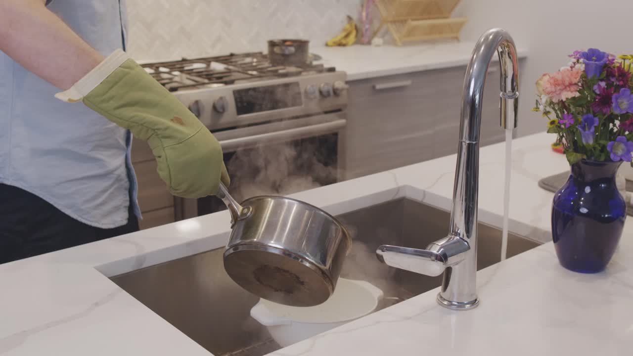 En slow motion optagelse af en gryde med dampende varm pasta, der hældes i en si i en køkkenvask