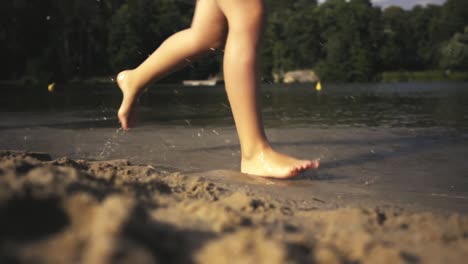 a girl and a boy running on a sandbar by a lake