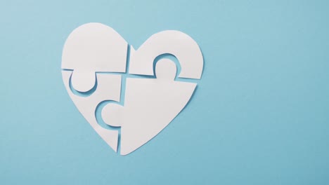 video of white jigsaw puzzle heart on blue background with copy space