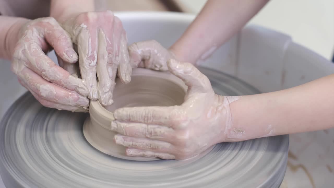 el maestro alfarero le enseña al niño a trabajar con arcilla en la rueda del alfarero.
