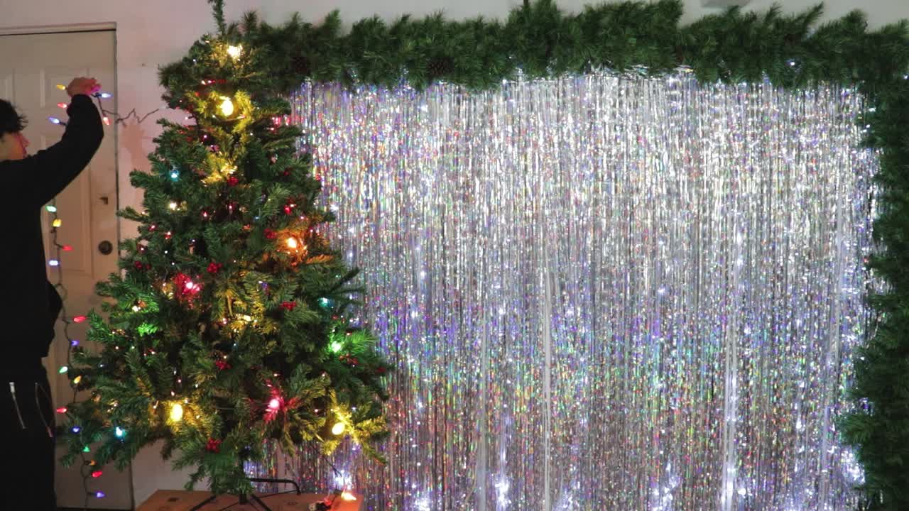 Man becorates christmas tree with colorful lights and ornaments