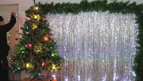 man becorates christmas tree with colorful lights and ornaments