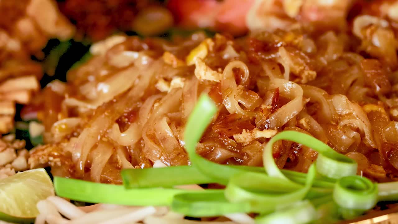 A detailed view of savory noodles topped with fresh green onions and lime wedges.