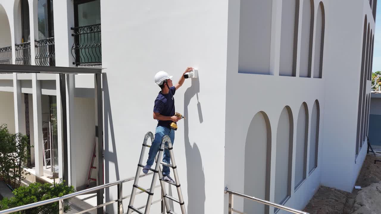 Man Installing a Security Camera on a White Building Wall