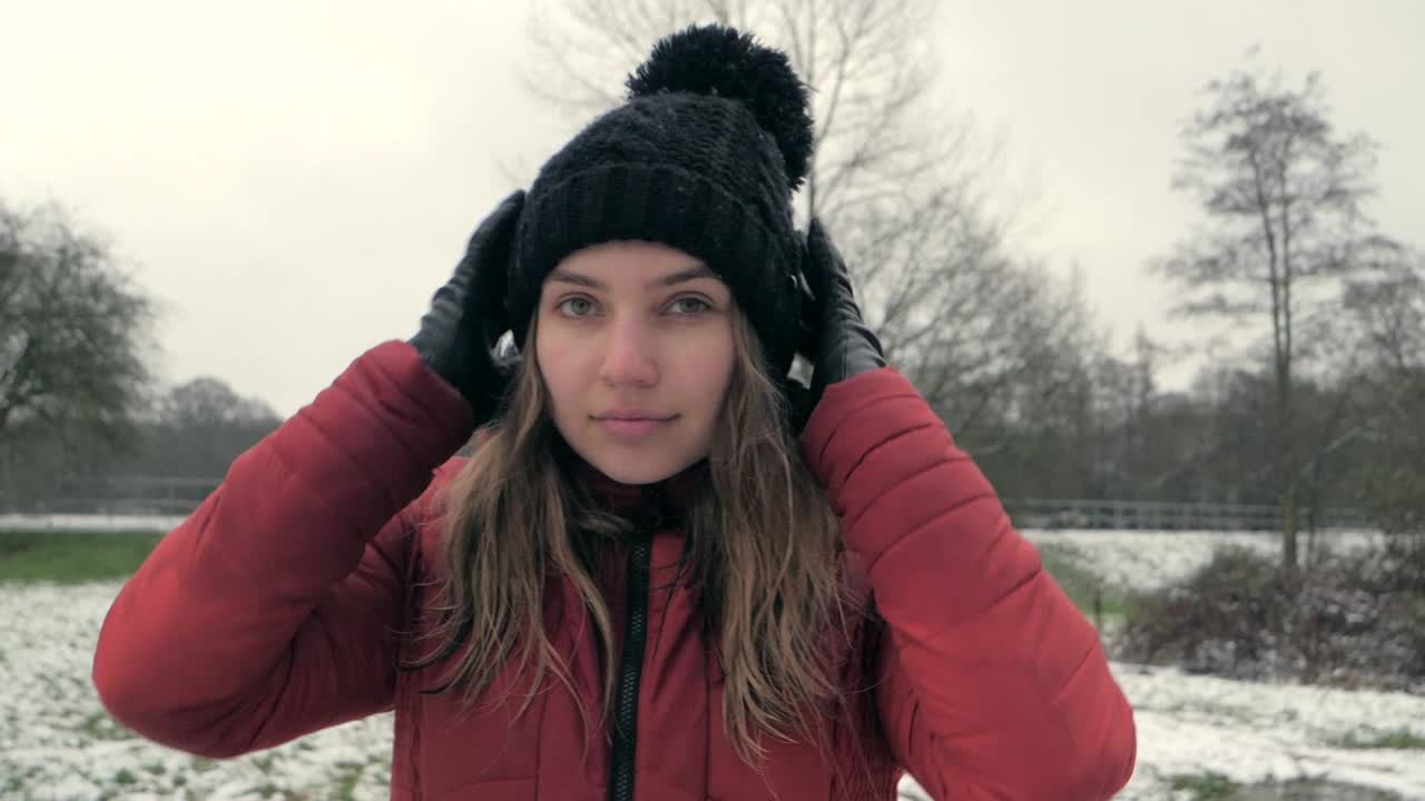 Front view of girl arranging her hat in slow motion during a snowy winter day.