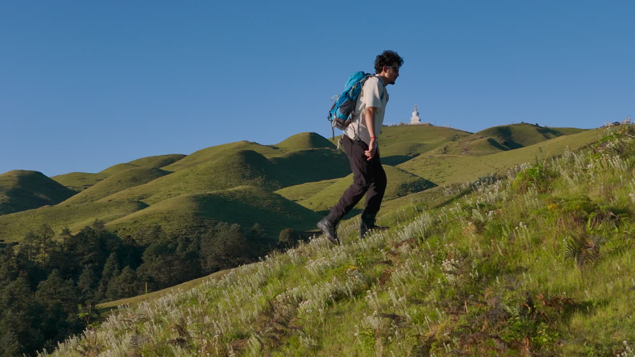 Drone shot of male hiker trekking through green hills and forests in Nepal Sailung Dolakha near Tibet blue sky backdrop, he enjoys peaceful environment while planning a camping escape in nature