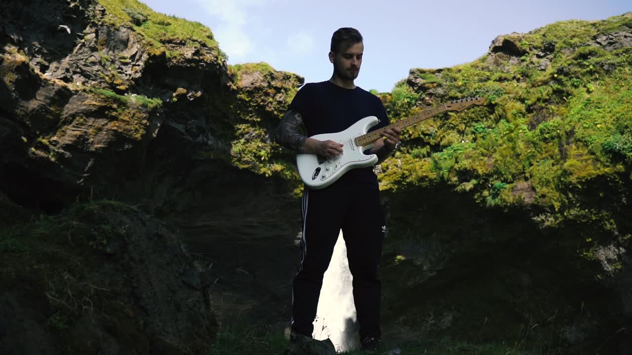 Uomo che suona la chitarra davanti a una bellissima cascata in Islanda