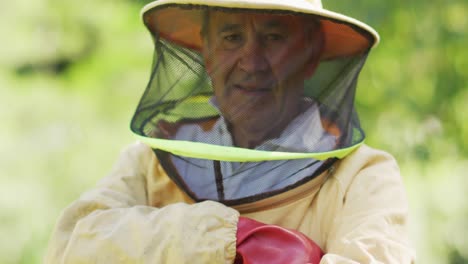 portrait of smiling caucasian male beekeeper in protective clothing with arms crossed