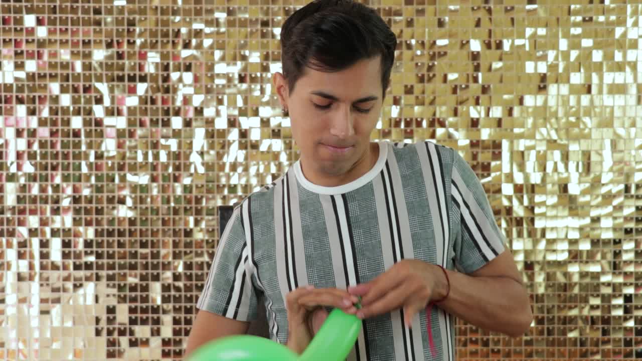 joven mexicano atando un globo verde con un telón de fondo dorado pared brillante