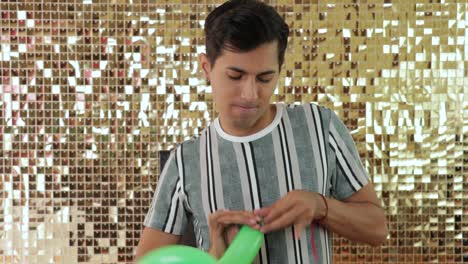 young mexican man tying green balloon with golden backdrop shimmer wall