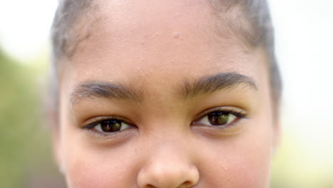 Retrato-De-Cerca-De-Ojos-Marrones-De-Una-Feliz-Chica-Afroamericana-Sonriendo-En-Un-Jardín-Soleado,-Cámara-Lenta