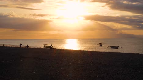 Silhouetted-running,-exercising-and-relaxing-on-beach-during-golden-sunset-overlooking-ocean-on-tropical-island-of-Timor-Leste