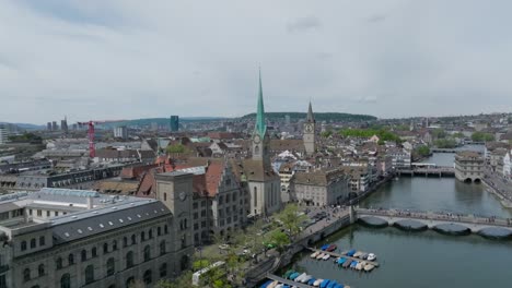 Slow-forward-moving-panning-drone-showing-city-inhabitants,-the-clock-towers,-public-transport-and-skyline-of-Zurich