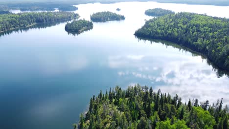 aerial footage of a lake with the sky's reflection and lots of green bush and trees