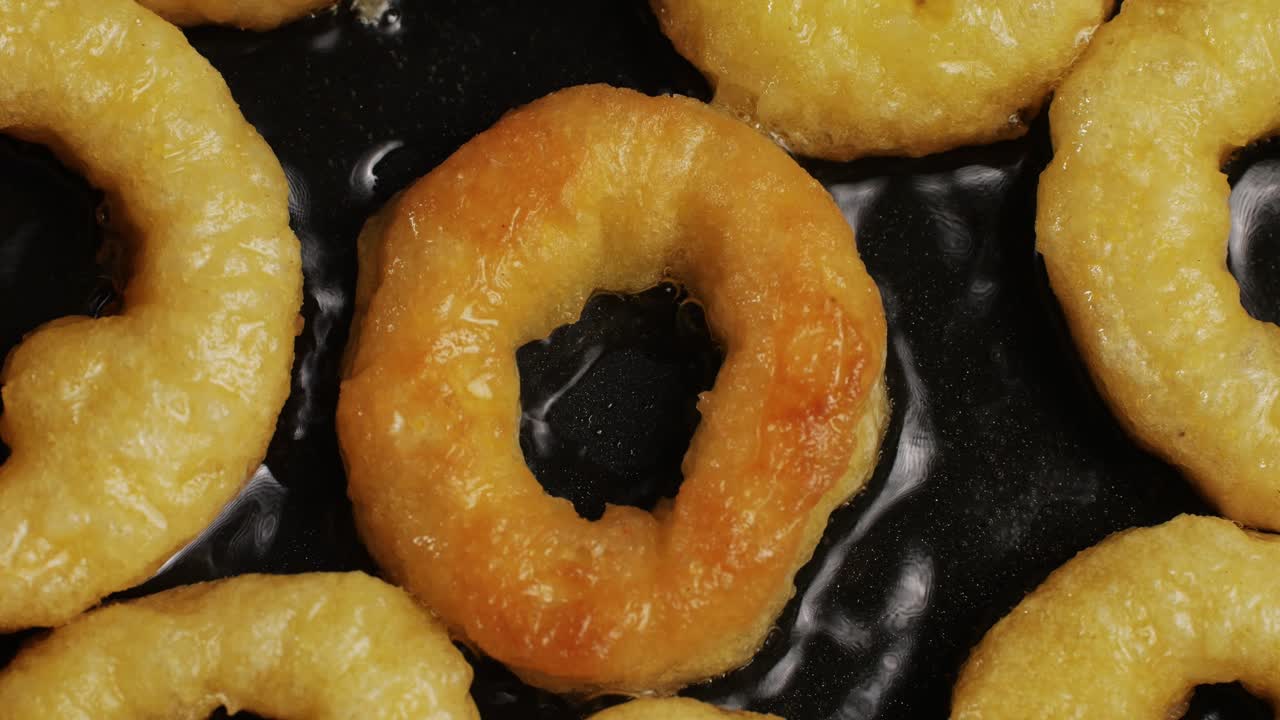 Fried crispy onion rings in a frying pan with boiling oil top view. Roasted onion rings for snacks at bar, cafe. Fast food. Delivery. Beer snacks