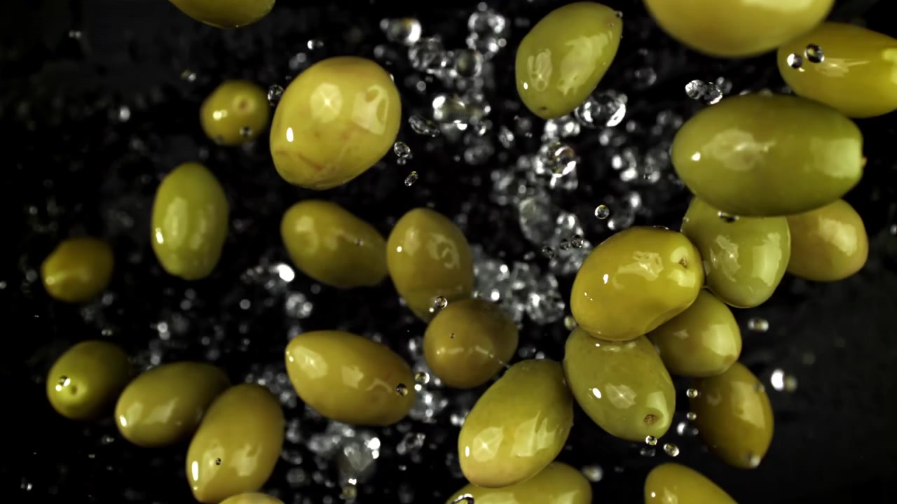Olive verdi che cadono al rallentatore con schizzi d'acqua
