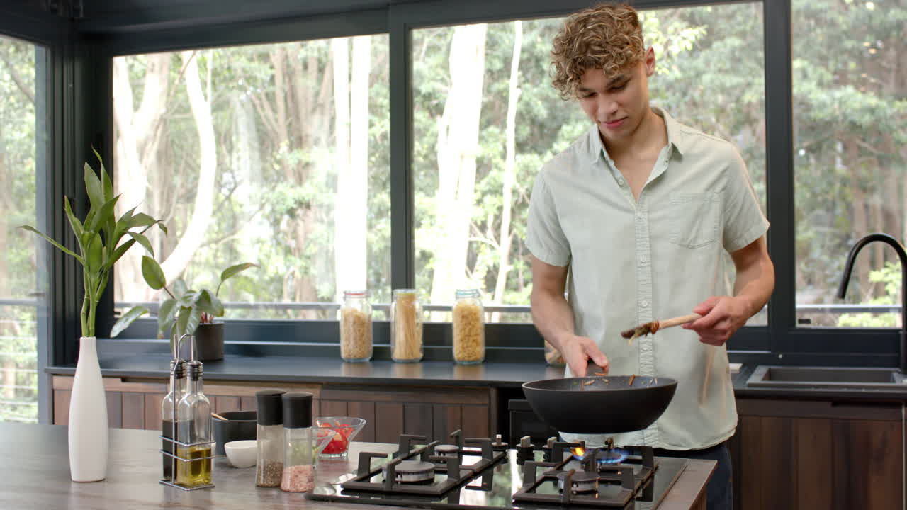 Young man cooking in modern kitchen, stirring vegetables in frying pan, copy space