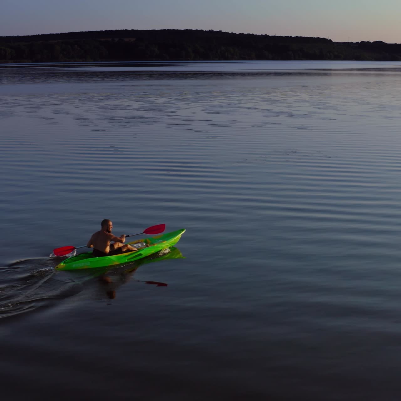 Young man kayaks on lake at sunset. Alone man riding on a rowing boat on the lake at dusk time. Man in a boat with oars in the evening. Aerial view.