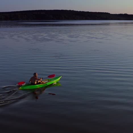 young man kayaks on lake at sunset. alone man riding on a rowing boat on the lake at dusk time. man in a boat with oars in the evening. aerial view.