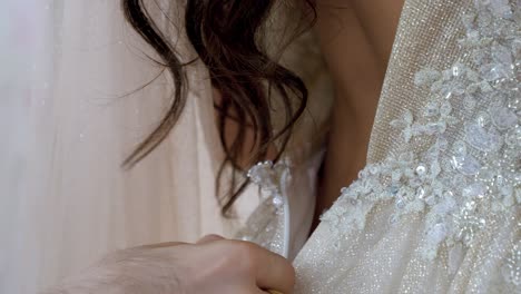 la mano delicada se cierra con gracia en la parte de atrás del exquisito vestido de novia de la novia.