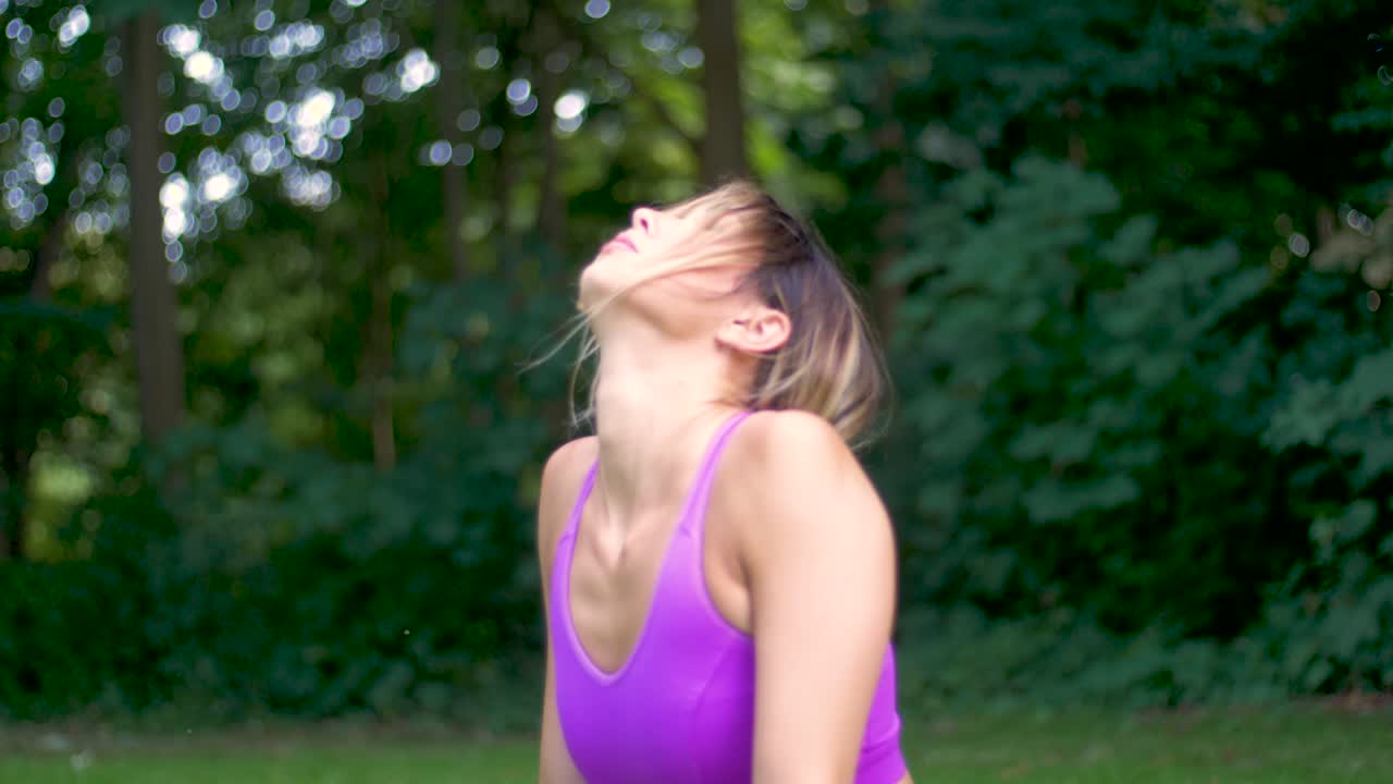Bella donna con lunghi capelli biondi che fa yoga all'aperto in un parco e si mette in posizione del cane a testa in su.