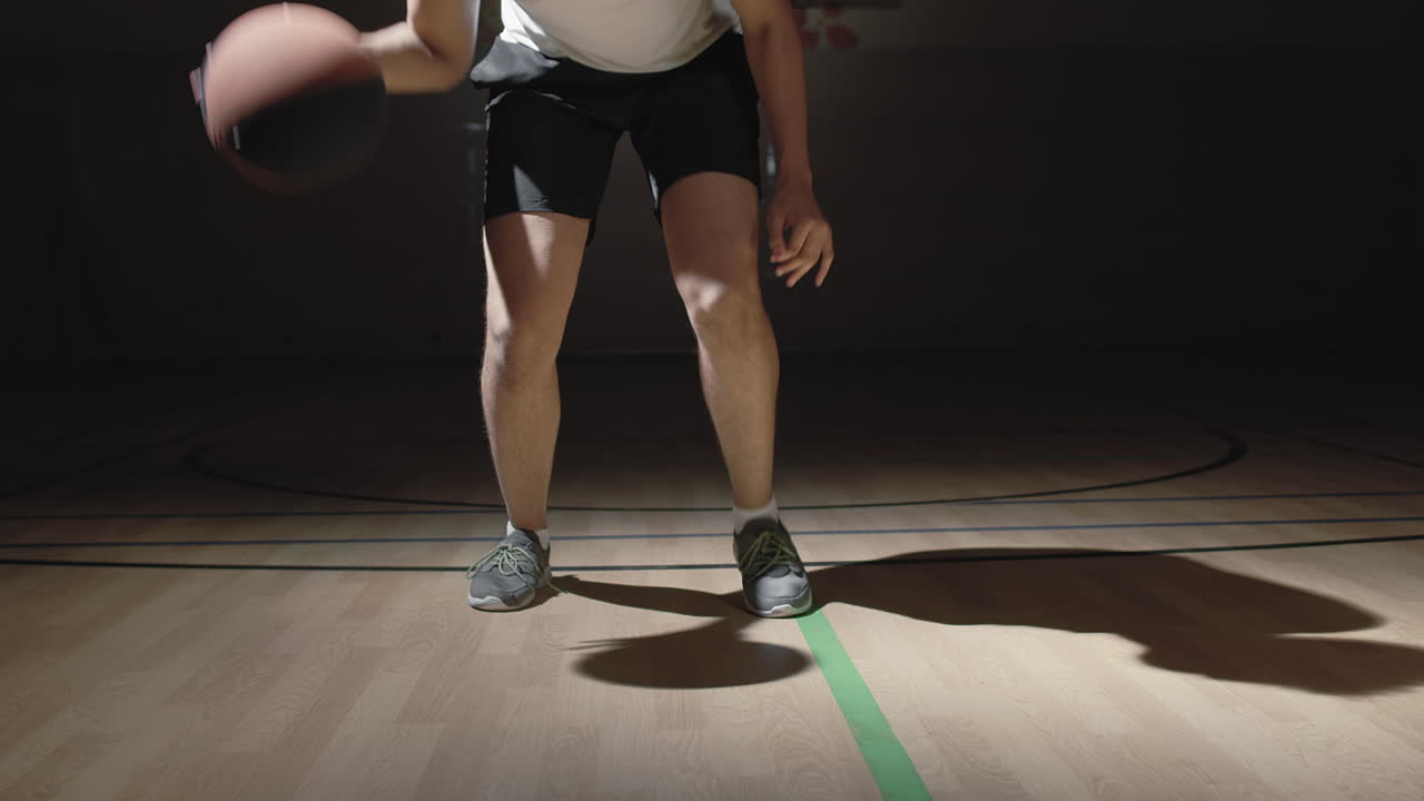 Male Basketball Player Dribbling Ball on Dark Court
