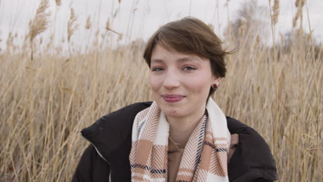 Nahaufnahme-Eines-Teenager-Mädchens-Mit-Kurzen-Haaren-Und-Winterkleidung,-Das-In-Die-Kamera-Schaut-Und-Ihr-Haar-In-Einem-Weizenfeld-Berührt