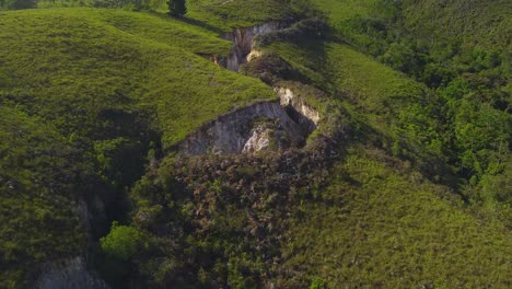 Drone-Vuela-Sobre-Grietas-Naturales-Ubicadas-En-Una-Montaña-Verdosa,-Durante-Una-Puesta-De-Sol