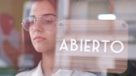 young sad woman changing open to closed sign in spanish on window for corona virus pandemic.