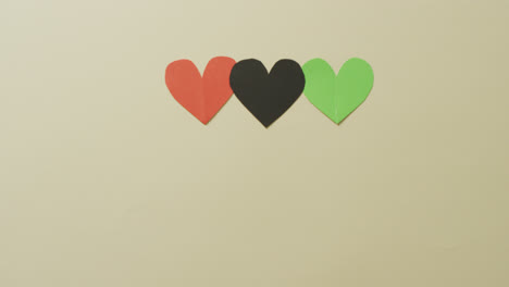 video of red, black and green paper hearts on beige background