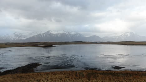 Wunderschöne-Isländische-Landschaft-Mit-Blick-Auf-Die-Berge-Mit-Einem-Silbrig-Reflektierenden-See-Und-Bewölktem-Himmel