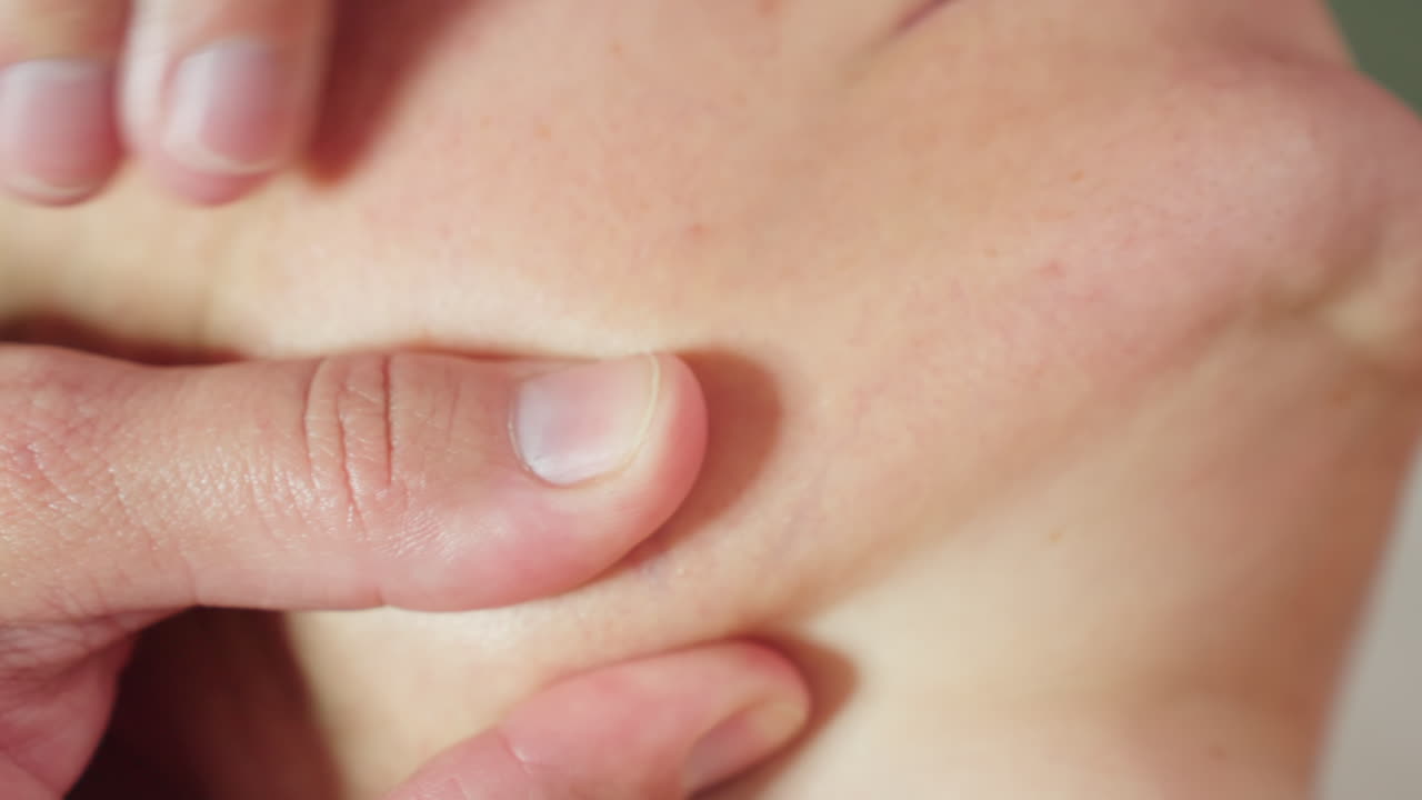 Skin Care Expert Cradles Client Jawline Applying Gentle Pressure With Fingertips During Relaxing Facial Massage Session Under Soft Clinical Lighting Beside Organized Product Trolley In Treatment Room