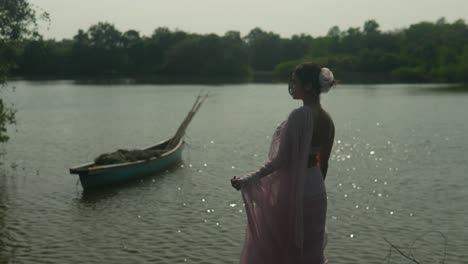 woman in vintage dress by river with canoe, reflecting, serene mood, daylight