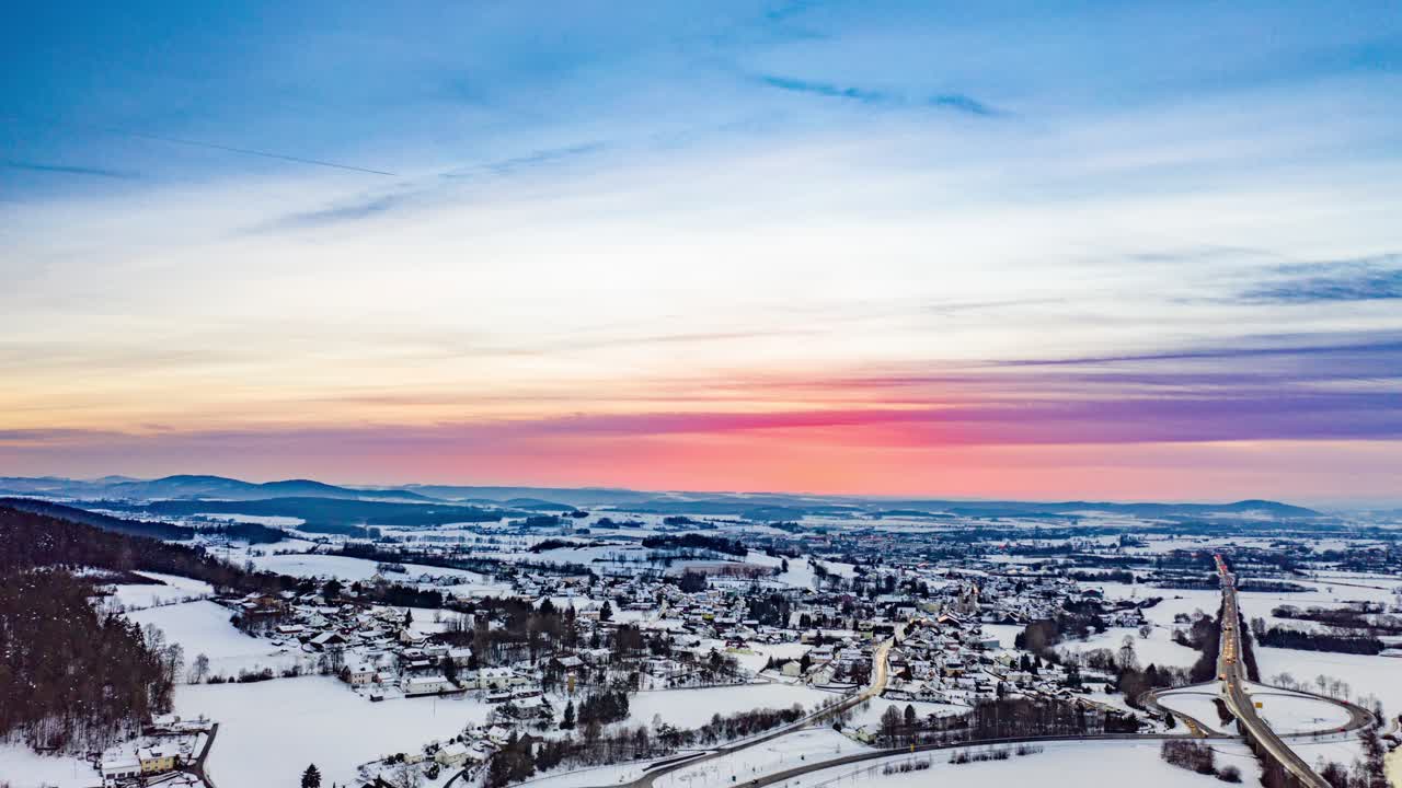 A beautiful sunset. The sun already retreated, some light still lingering on the sky coloring the horizon in all shades of pink, yellow and orange. White clouds above the densely populated valley