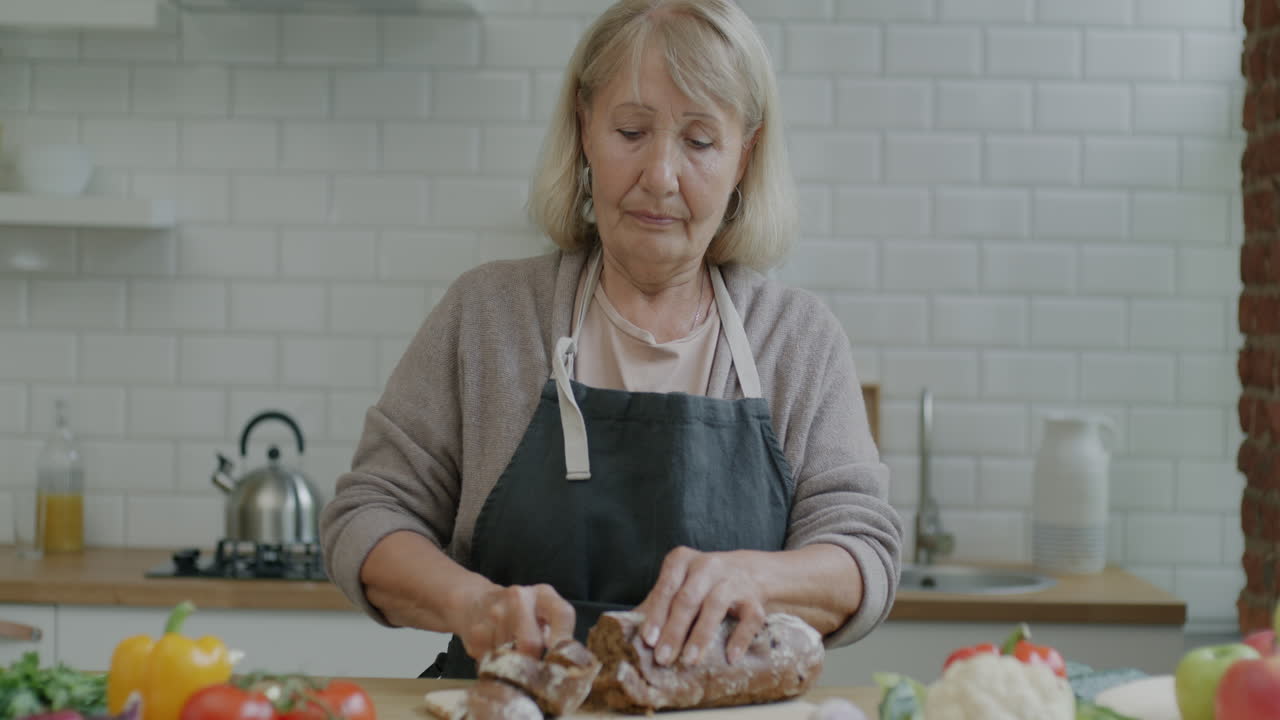 Elderly Woman Cutting Bread in Kitchen
