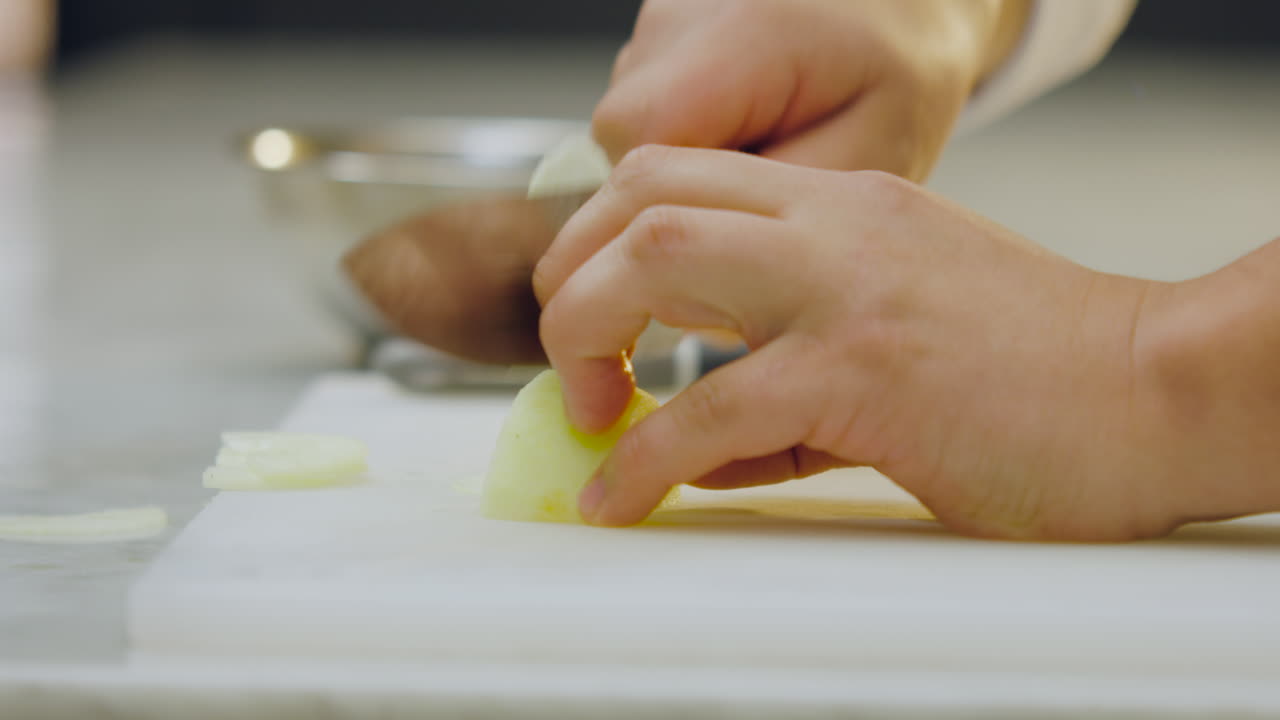 Close-up of a chef's hands cutting a peeled green apple into thin slices on a white chopping board and carefully placing them in an aluminum mold on a kitchen counter