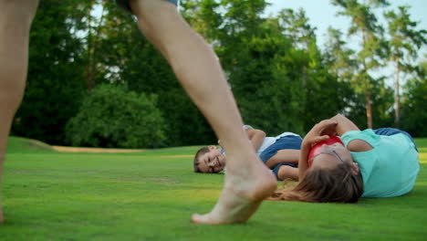 boy and girl lying on grass in field. father and kids playing with ball in park