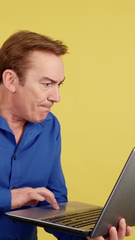 man reacting while using laptop on yellow background
