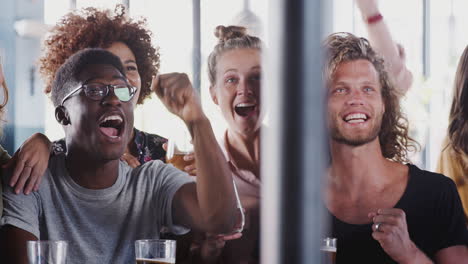 group of male and female friends celebrating whilst watching game on screen in sports bar